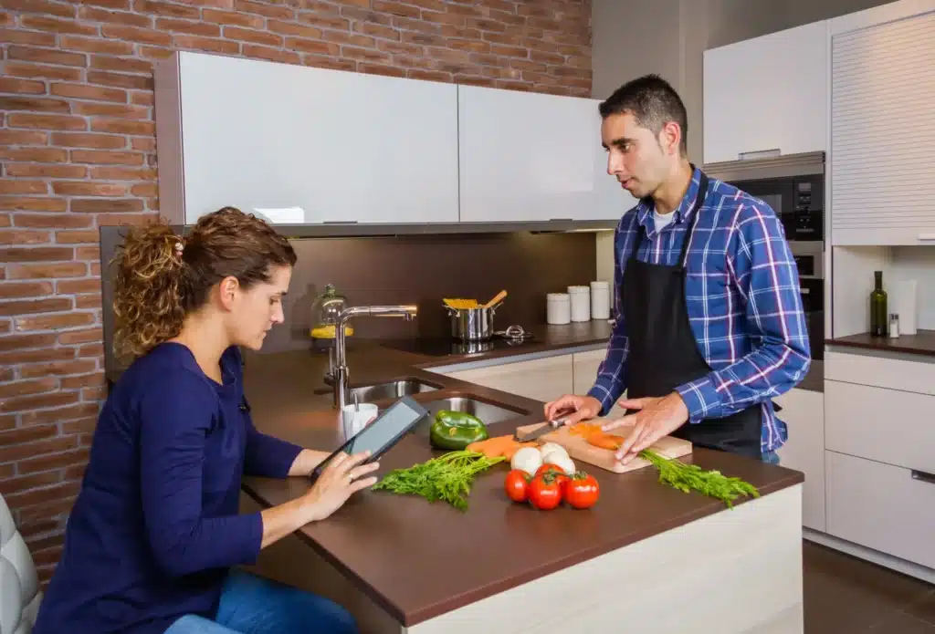 Un homme consulte une tablette en cuisinant dans une cuisine moderne.