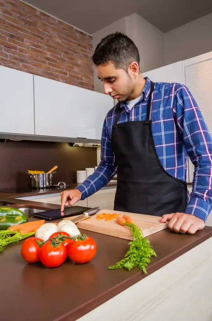 Marc consulte une tablette en cuisinant dans une cuisine moderne.
